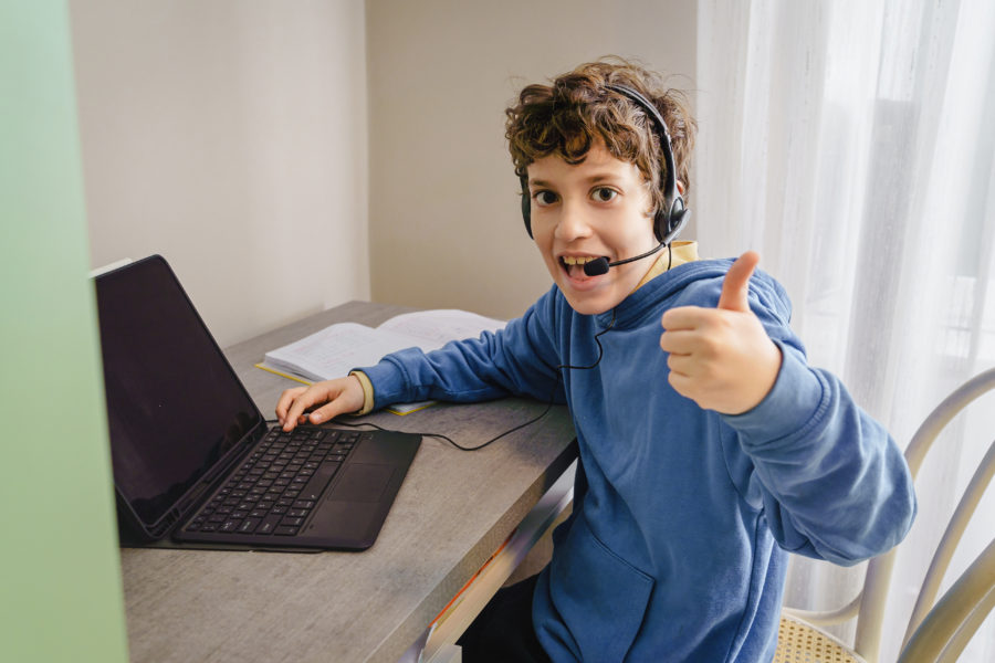 Kid with thumbs up remote learning on his desk using a tablet co